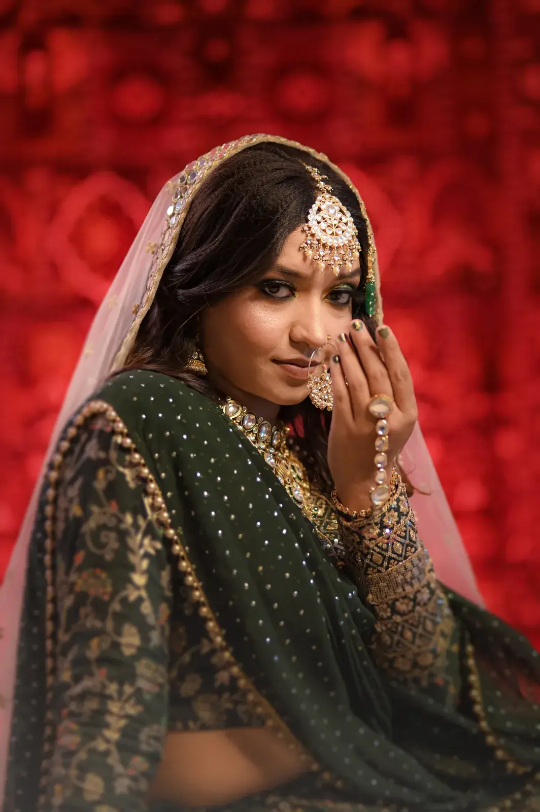 Bride in a dark green dupatta with gold work against a red backdrop