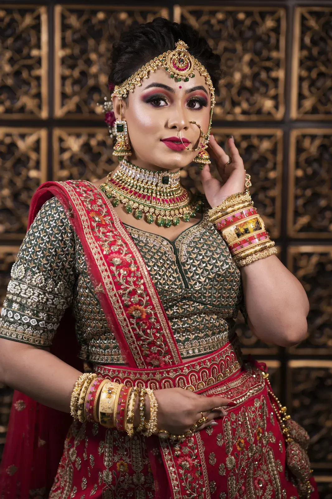 Bride in a green and red lehenga with a heavy choker, hand at her earring