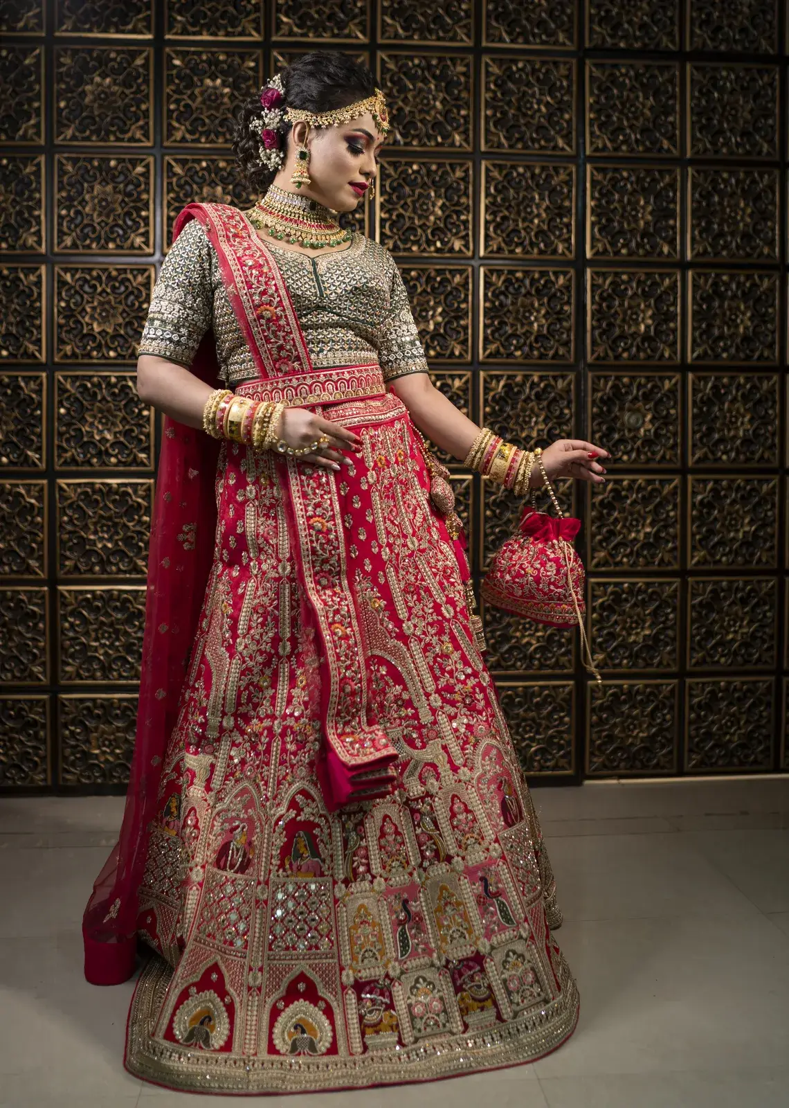 Full-length bride in an embroidered green and red lehenga holding a potli bag