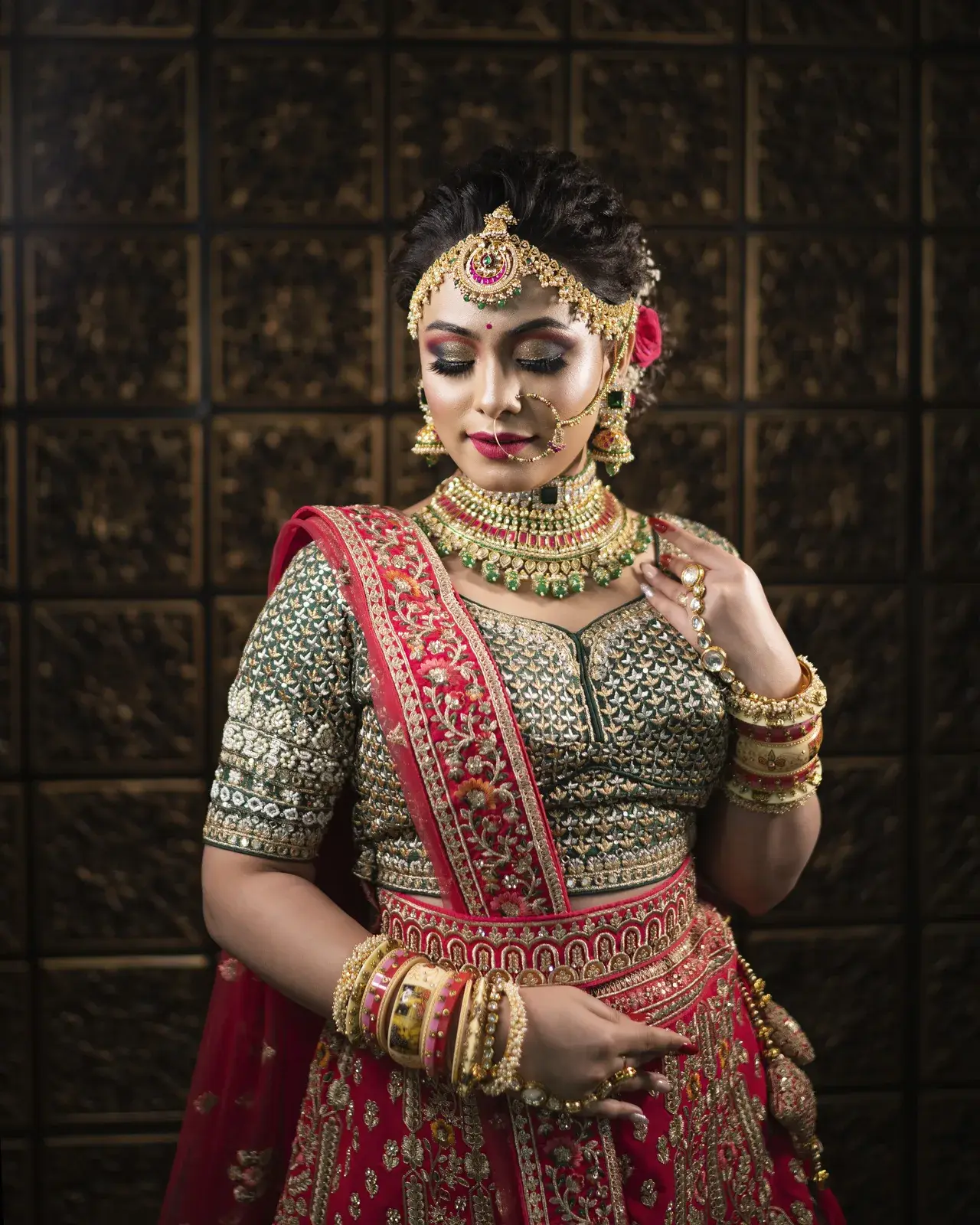Bride in a green blouse and red lehenga standing against a carved wooden screen