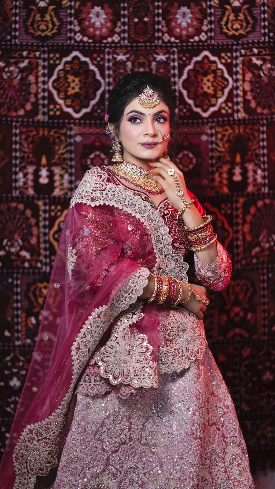 Full-length bride in a magenta lehenga in front of a patterned carpet