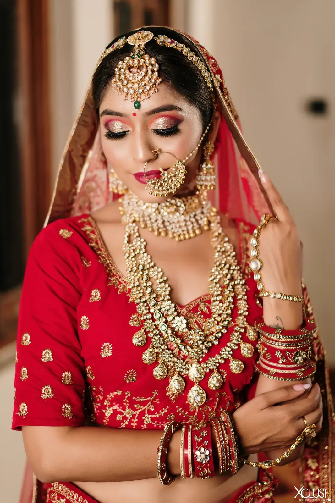 Bride in a red dupatta with a kundan necklace set and nath, eyes lowered