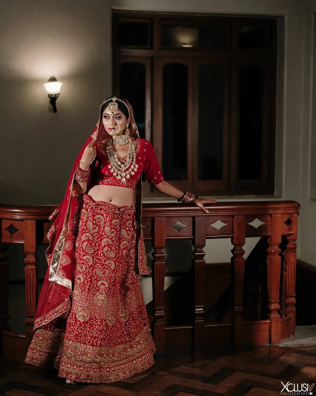 Full-length bride in a red lehenga on a wooden staircase