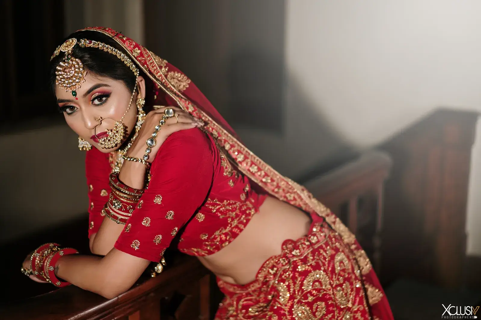 Bride in red leaning by a window and looking at the camera