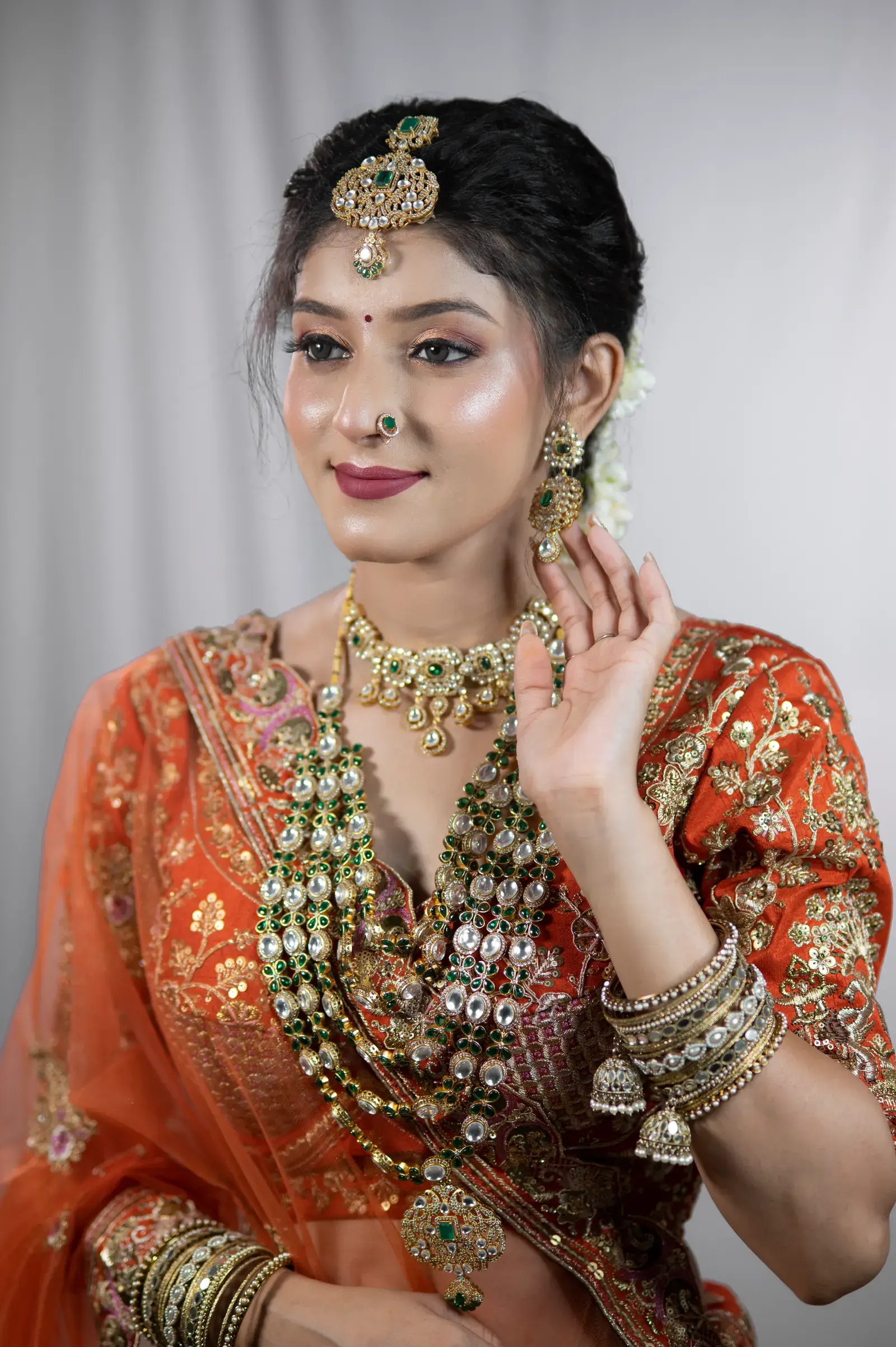 Bride in an orange lehenga with layered green-stone necklaces