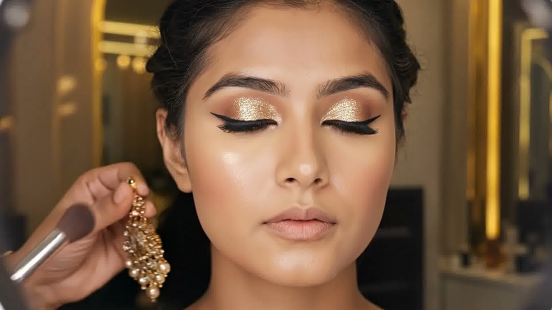 A kundan earring and a makeup brush held beside a woman with closed eyes and gold glitter eyeshadow