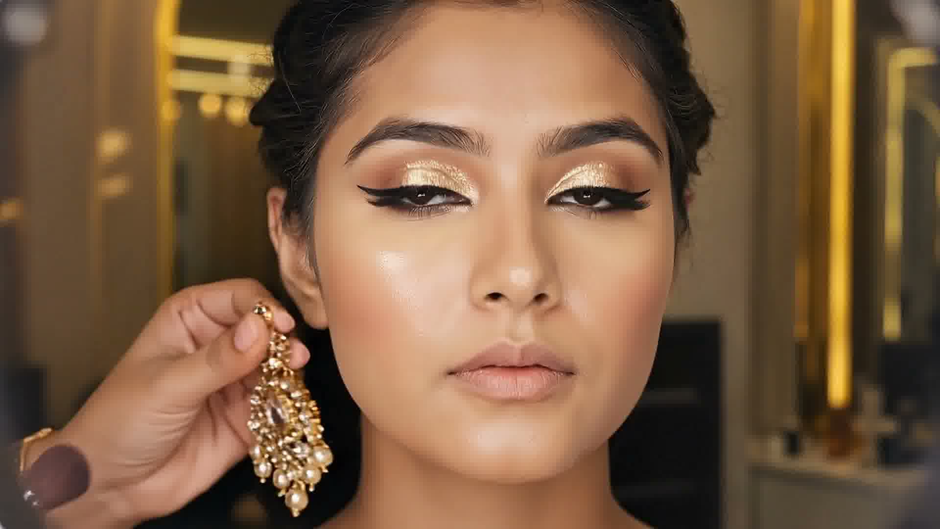 A kundan earring held up beside a woman wearing gold glitter eyeshadow and winged liner