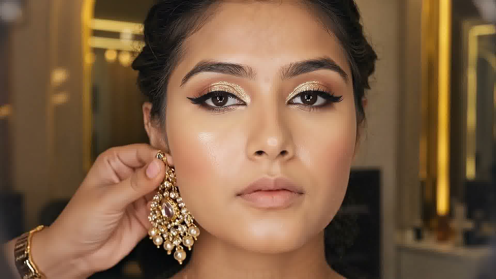 A kundan earring being fastened on a woman's ear during her bridal makeup
